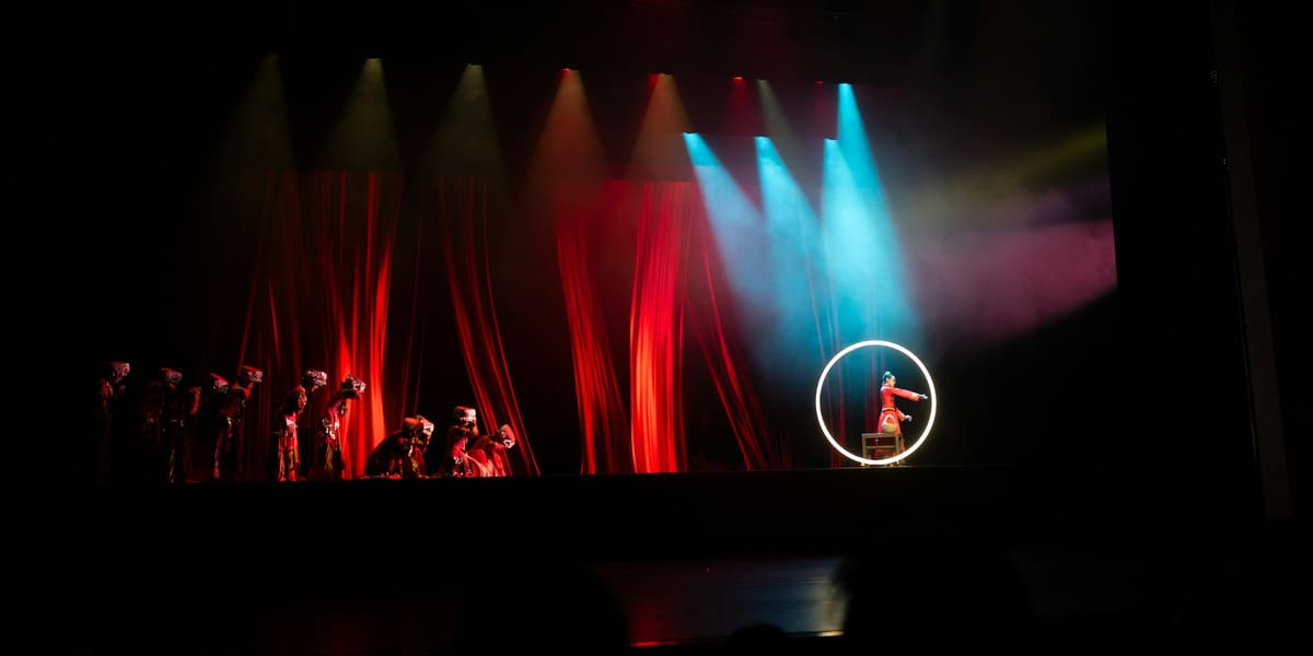 A performer inside a glowing hoop on a dark stage with red curtains and colored spotlights
