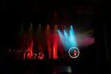 A performer inside a glowing hoop on a dark stage with red curtains and colored spotlights