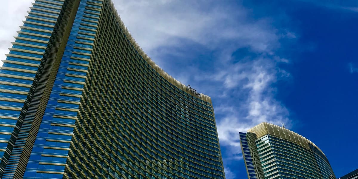 ARIA's curved glass hotel towers rising against a blue sky with wispy clouds