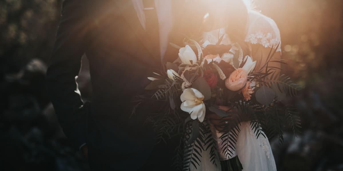 Backlit bride and groom standing close together, the bride holding a bouquet, lit by golden sunset light
