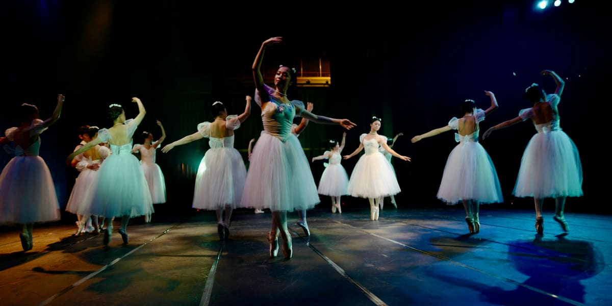 Ballet dancers in white tutus performing on a dark stage under spotlights
