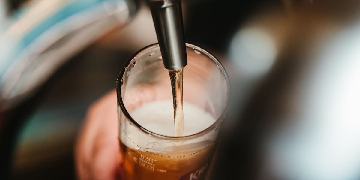 Close-up of golden beer being poured from a tap into a tall glass with foam rising