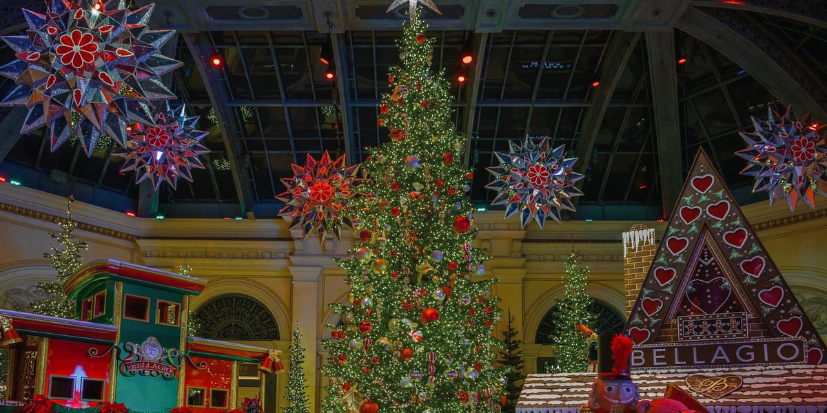 A lit Christmas tree, toy train, gingerbread house and hanging star lanterns in the Bellagio Conservatory