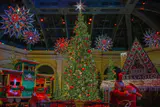 A lit Christmas tree, toy train, gingerbread house and hanging star lanterns in the Bellagio Conservatory