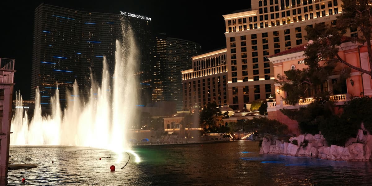 Fountain jets rising from the Bellagio lake at night, with the Bellagio and Cosmopolitan towers behind