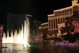 Fountain jets rising from the Bellagio lake at night, with the Bellagio and Cosmopolitan towers behind