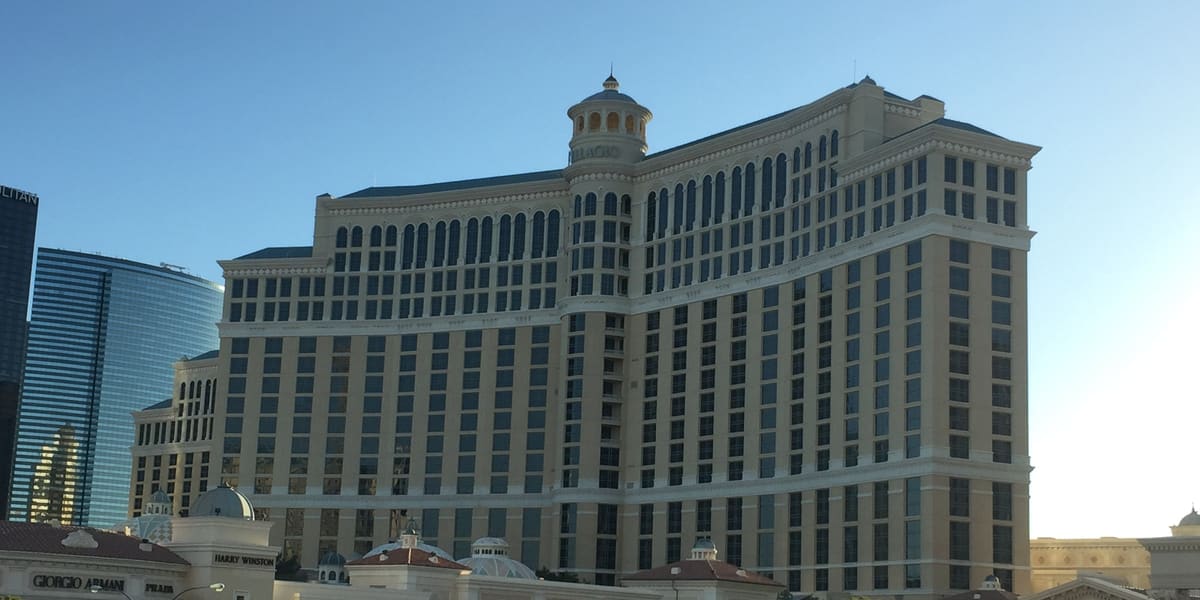 Bellagio's curved cream-colored hotel tower under a clear blue sky, with lower Strip buildings in front
