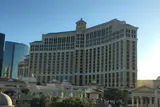 Bellagio's curved cream-colored hotel tower under a clear blue sky, with lower Strip buildings in front