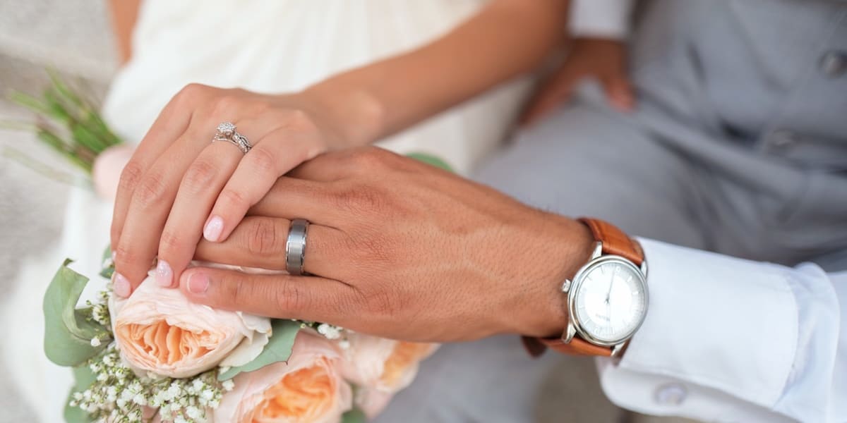 Close-up of a bride and groom's hands resting together on a bouquet, showing their wedding rings