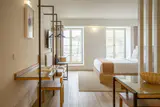 Bright, clean hotel room with a made bed, desk, light wood floor and tall windows