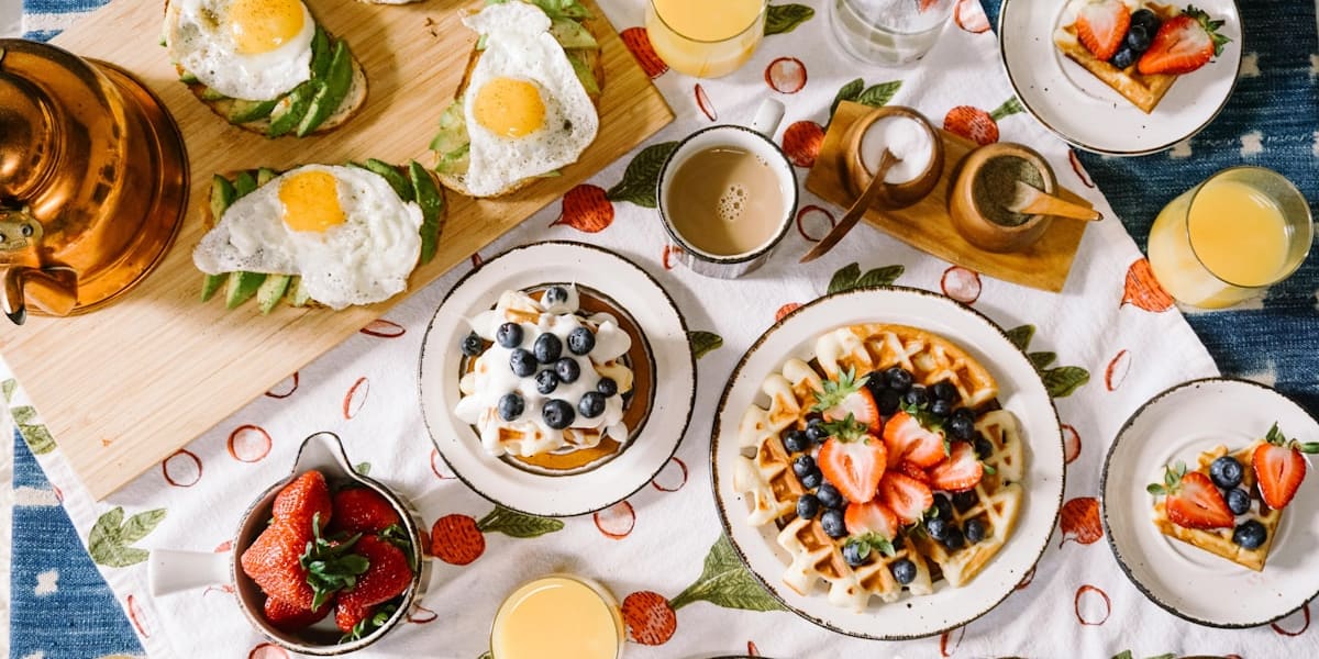 Overhead brunch table with waffles, fried-egg avocado toast, mimosas, coffee and strawberries