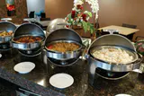 A row of open stainless steel chafing dishes holding hot food on a buffet counter