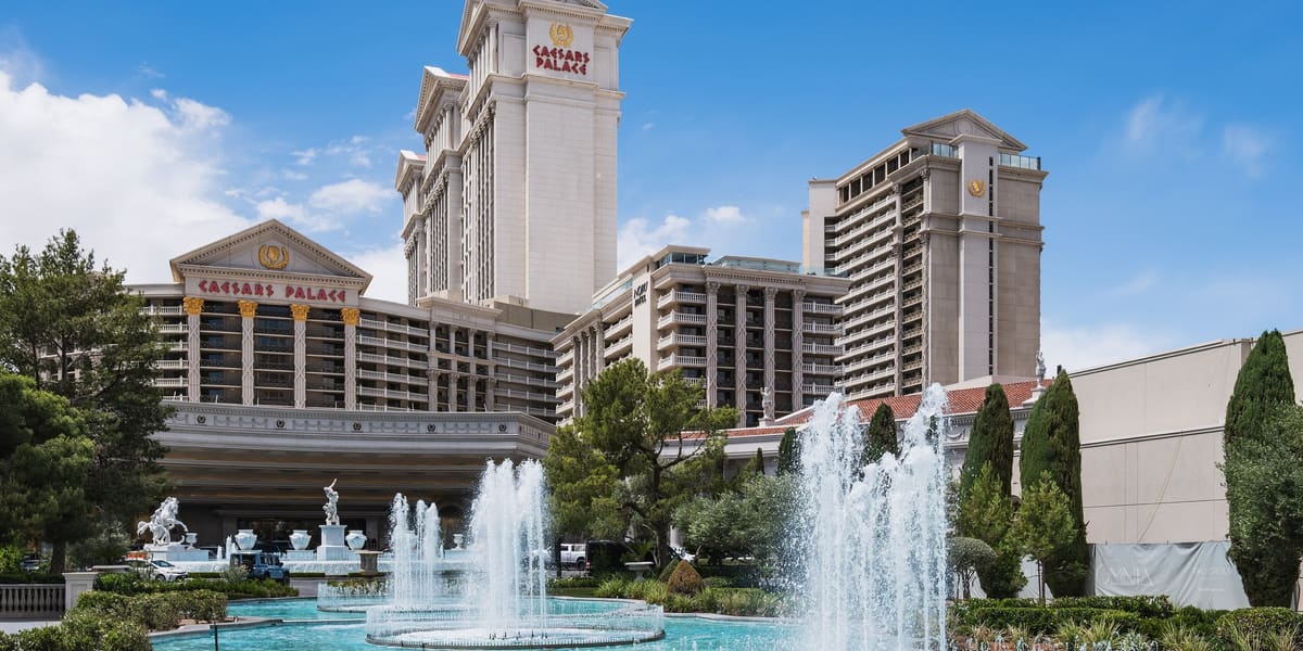 Caesars Palace hotel towers behind turquoise fountain pools and cypress trees on a sunny day