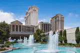 Caesars Palace hotel towers behind turquoise fountain pools and cypress trees on a sunny day