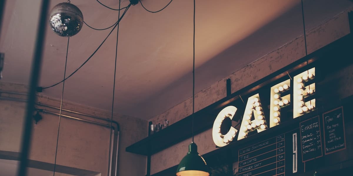 Cafe interior with a lit marquee CAFE sign, green pendant lamps and a hanging disco ball