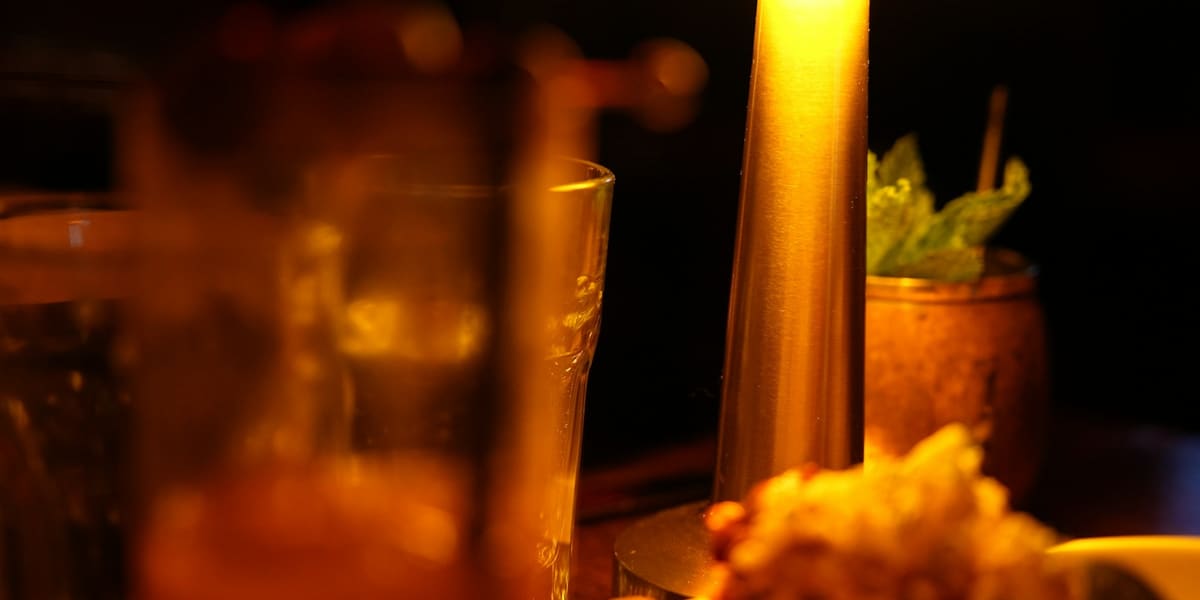Cocktails and a small plate on a dimly lit table under the warm glow of a table lamp