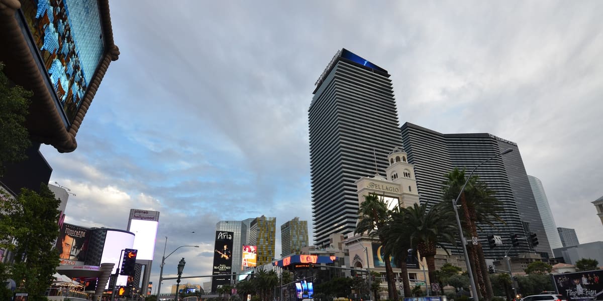 The Cosmopolitan's tall glass towers seen from a busy Las Vegas Boulevard sidewalk under a cloudy sky