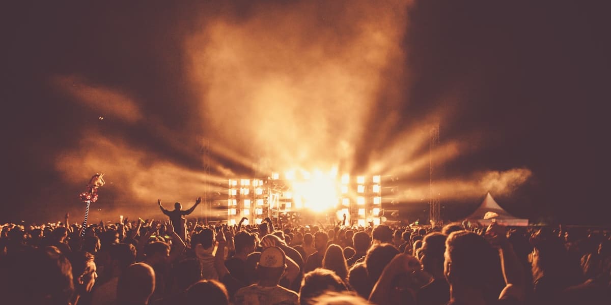 Dense festival crowd with arms raised facing a brightly lit stage and smoke at night