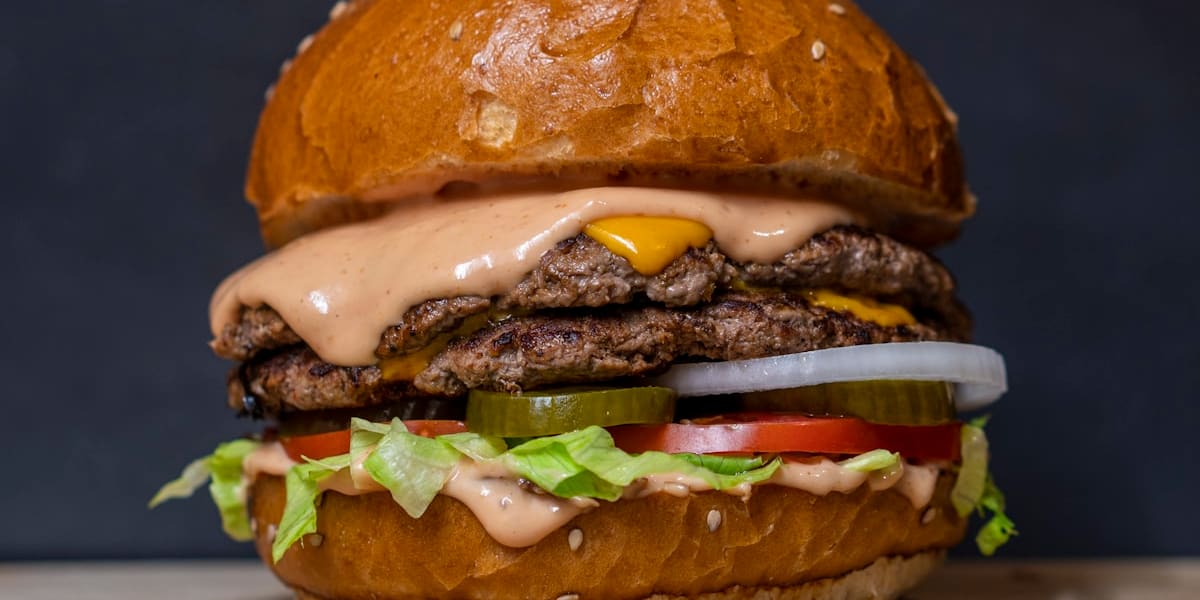 Close-up of a double cheeseburger with melted cheese, lettuce, tomato, pickle slices and onion