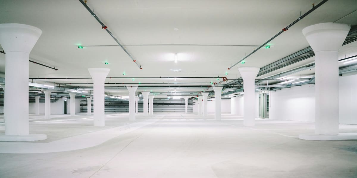 Empty white concrete parking garage level with rows of round pillars and overhead lights