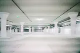 Empty white concrete parking garage level with rows of round pillars and overhead lights