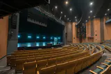 Curved rows of empty wooden theater seats facing a stage lit with blue lights