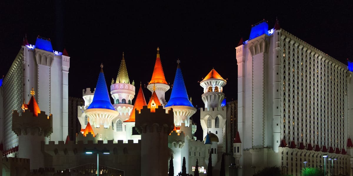 Excalibur's lit castle turrets with blue and orange spires between two white hotel towers at night