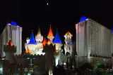 Excalibur's lit castle turrets with blue and orange spires between two white hotel towers at night