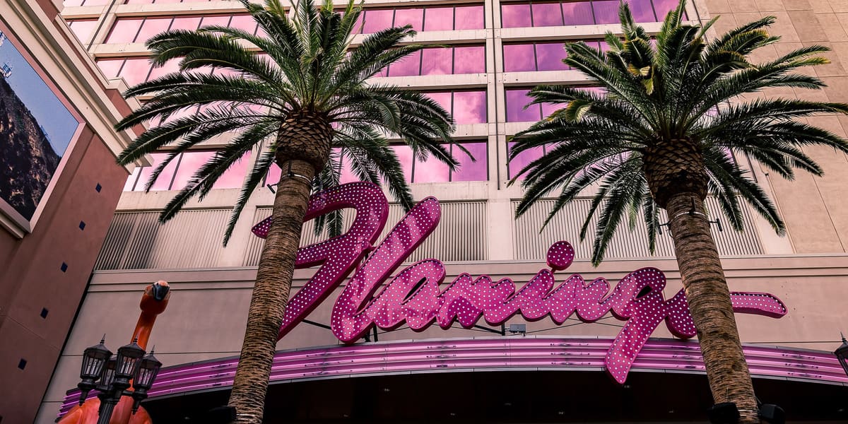Pink neon Flamingo script sign between two palm trees in front of the hotel's pink-windowed facade