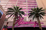 Pink neon Flamingo script sign between two palm trees in front of the hotel's pink-windowed facade