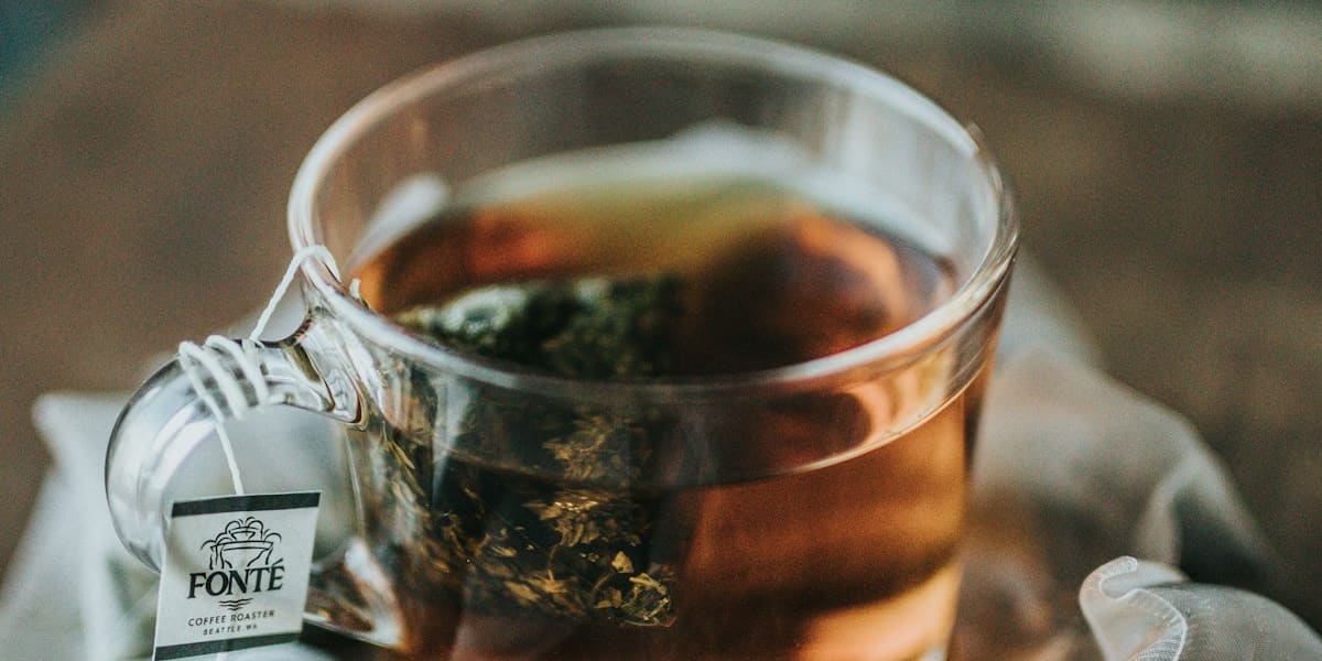Glass teacup of brewed tea surrounded by loose-leaf pyramid tea bags on a wooden table