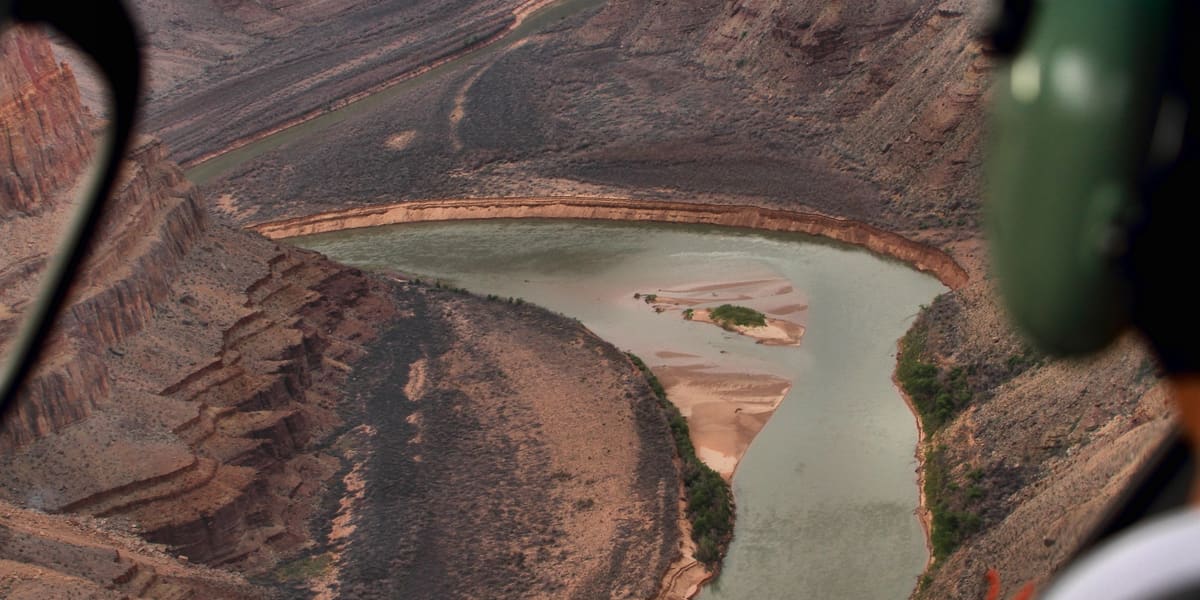 The river and canyon walls seen through a helicopter window, with a passenger headset in the foreground