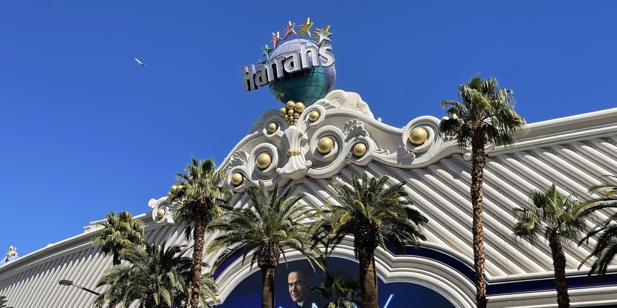 White ornate facade of Harrah's Las Vegas with its globe sign, palm trees and a show billboard