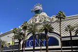 White ornate facade of Harrah's Las Vegas with its globe sign, palm trees and a show billboard