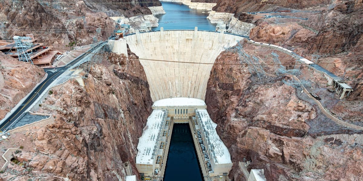 Hoover Dam's concrete arch and powerhouses in Black Canyon, seen from above with Lake Mead behind
