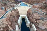 Hoover Dam's concrete arch and powerhouses in Black Canyon, seen from above with Lake Mead behind