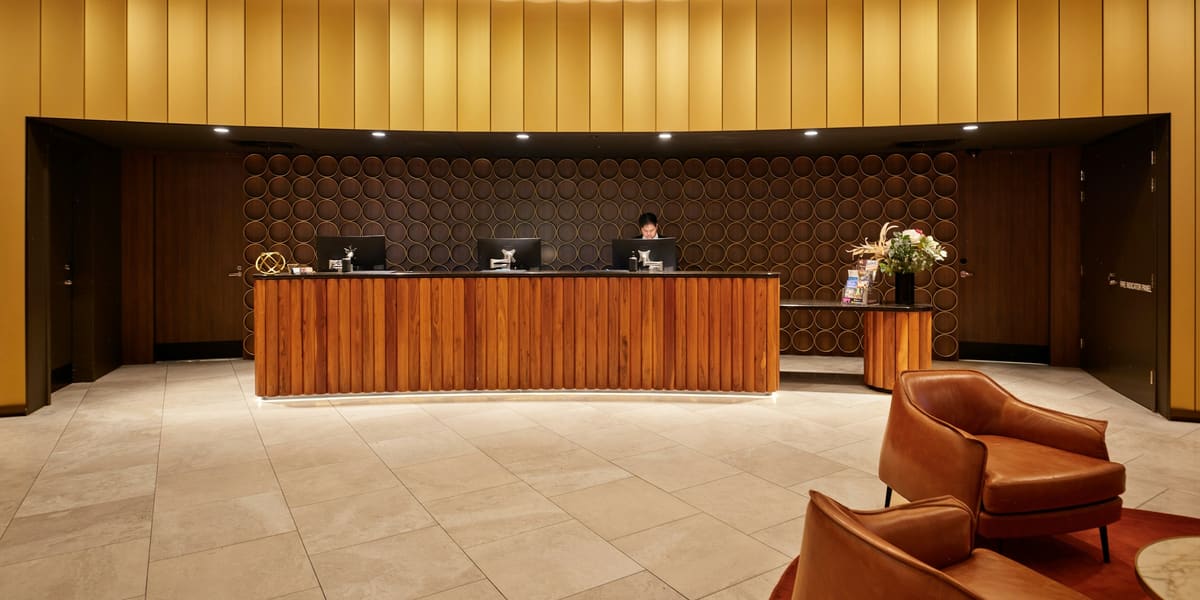 Hotel reception desk with wood panelling, a staff member at a computer and leather lobby armchairs