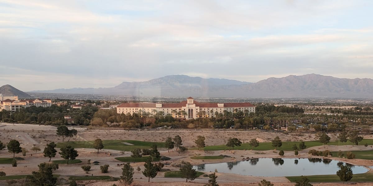 Red-roofed JW Marriott and Rampart Casino buildings beyond a golf course with mountains behind