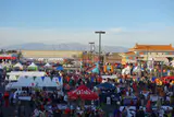 Crowds among food stalls and tents in the Chinatown Plaza parking lot, with pagoda-style roofs and mountains beyond