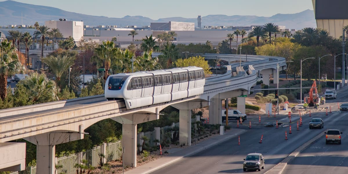 White Las Vegas Monorail train on an elevated curved track beside a road lined with palm trees