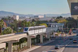 White Las Vegas Monorail train on an elevated curved track beside a road lined with palm trees