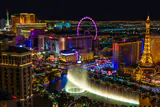 Las Vegas skyline at night from above, with lit fountains, an observation wheel and an Eiffel Tower replica
