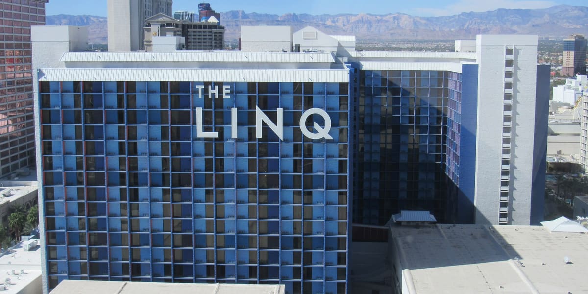 The LINQ hotel tower's blue-panelled facade and sign, seen from above with mountains in the distance