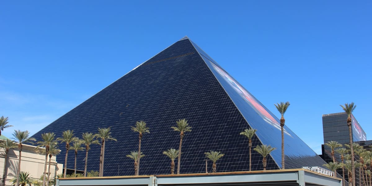 Black glass pyramid of the Luxor hotel behind palm trees under a clear blue sky