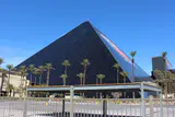 Black glass pyramid of the Luxor hotel behind palm trees under a clear blue sky