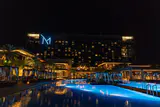M Resort hotel tower lit at night behind a blue-lit pool lined with cabanas