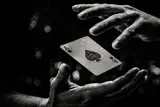 Black and white close-up of two hands appearing to levitate an ace of spades playing card