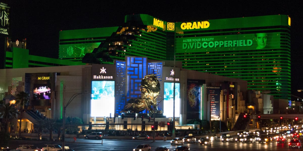 MGM Grand's green-lit hotel tower and lion statue at night, with traffic on the boulevard
