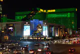 MGM Grand's green-lit hotel tower and lion statue at night, with traffic on the boulevard
