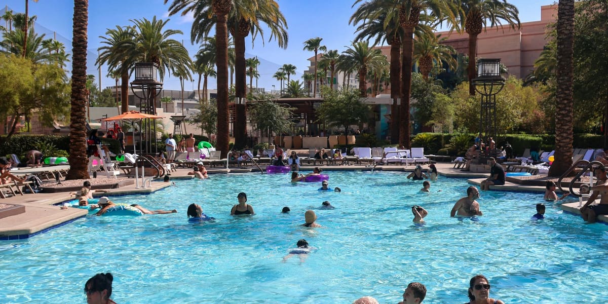 Swimmers in a large resort pool ringed by palm trees and loungers under a clear blue sky at MGM Grand